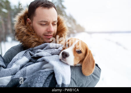 Un jeune homme passa son meilleur ami chien beagle dans une couverture chaude pour réchauffer lui dans une neige froide de l'hiver. La protection des animaux Banque D'Images