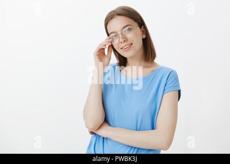 Me dire quelque chose d'intéressant, l'écoute attentivement. Portrait of confident female freelancer dans le quartier branché de lunettes, lunettes de rim toucher et tilting head, debout avec bras croisés sur la poitrine Banque D'Images