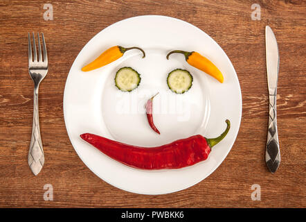 Piment et tranches de concombre sous forme de sourire sur une plaque blanche avec des ustensiles de cuisine Vue de dessus Banque D'Images