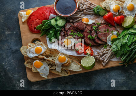 Repas Petit-déjeuner télévision divers laïcs. Vue de dessus sur planche de bois buffet avec de la viande, œufs, légumes, pain, etc Banque D'Images