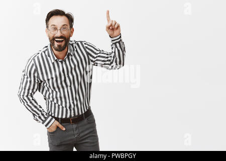 L'homme est heureux de tout. Portrait d'impressionné et amusé de belles affaires à chemise rayée et pantalon, se pencher vers la caméra en parlant de point, pointant vers le haut et tout sourire Banque D'Images