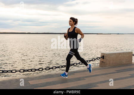 Jeune et jolie jeune fille tournant au coucher du soleil dans le parc de la ville. Remise en forme santé femme tournant à l'extérieur. Fleuve Amour à Khabarovsk horizon dans l'arrière-plan. Banque D'Images