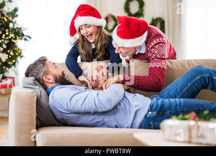 Une petite fille et de son grand-père avec Santa hat réveiller son père dormir sur un canapé à l'époque de Noël. Banque D'Images