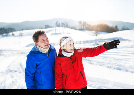 Senior couple porteur debout à l'extérieur en hiver, la nature se repose. Banque D'Images