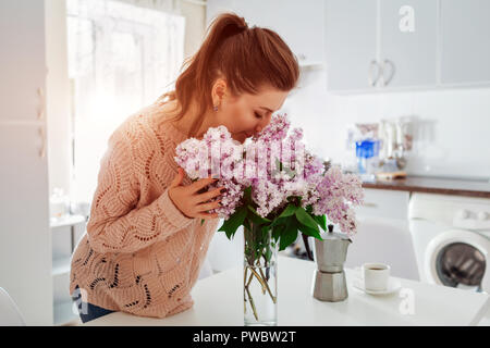 Allergie libre. Happy young woman smelling lilac dans une cuisine moderne. Concept d'allergies saisonnières. Banque D'Images