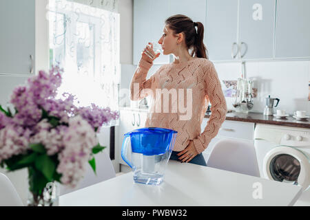 Femme buvant de l'eau filtrée du filtre verseuse en cuisine. Conception de la cuisine moderne. Concept de vie sain. Banque D'Images