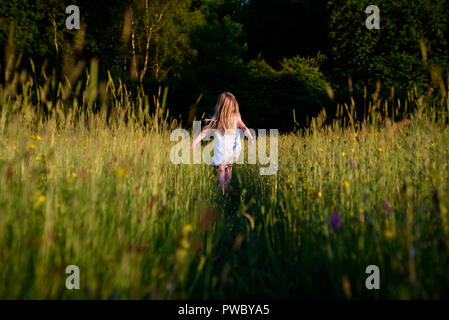 Jeune fille en fuite, grâce à wild flower meadow, vers les bois. Banque D'Images