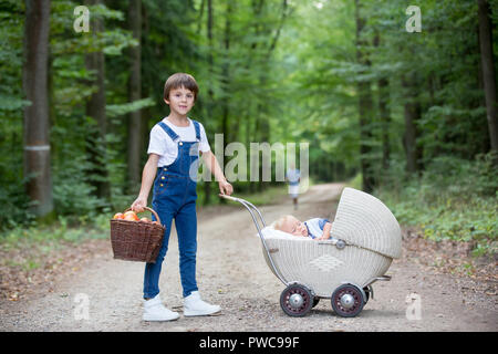 Peu de nouveau-né garçon et ses frères plus âgés en forêt, ancienne rétro baby poussette, temps d'automne Banque D'Images