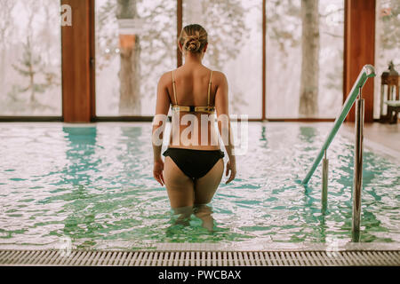 Jolie jeune femme d'entrer dans l'eau à une piscine dans le centre de spa Banque D'Images