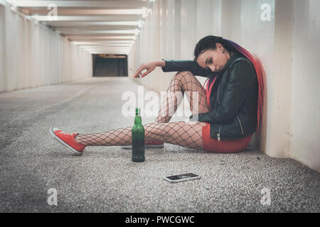 Jeune fille déprimée de boire de l'alcool et du tabac dans le souterrain dans l'attente d'appel important. femme regarde l'écran du smartphone avec un Banque D'Images