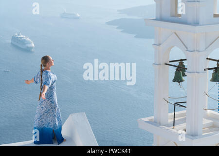 Happy woman in white dress bleu et profiter de ses vacances à Santorin, Grèce. Vue sur la caldeira et la mer Égée d'Imerovigli. Banque D'Images