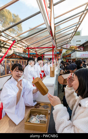 Nouvel An japonais, shogatsu. Shrine Maidens, Miko, occupé à lutter contre la vente de papier des feuillets d'omikuji fortune à Ikuta Temple Shinto à Kobe. Banque D'Images