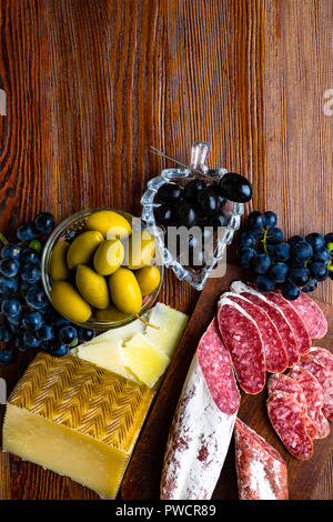 Mélange de différentes collations et des apéritifs. Des tapas espagnoles sur une plaque de bois. Bar à tapas de chorizo., olives, saucisson, fromage, raisin. Vue d'en haut Banque D'Images