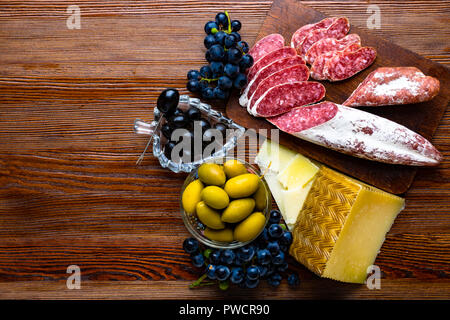 Mélange de différentes collations et des apéritifs. Des tapas espagnoles sur une plaque de bois. Bar à tapas de chorizo., olives, saucisson, fromage, raisin. Vue d'en haut Banque D'Images