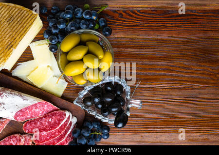 Mélange de différentes collations et des apéritifs. Des tapas espagnoles sur une plaque de bois. Bar à tapas de chorizo., olives, saucisson, fromage, raisin. Vue d'en haut Banque D'Images