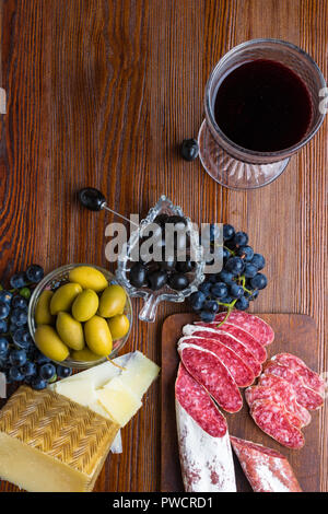 Plateau avec des tranches de fromage pecorino toscano dur italien, de la viande séchée de salami, de verre de vin rouge, le raisin, les olives sur planche de bois, snack-bar Banque D'Images