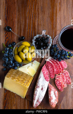 Plateau avec des tranches de fromage pecorino toscano dur italien, de la viande séchée de salami, de verre de vin rouge, le raisin, les olives sur planche de bois, snack-bar Banque D'Images