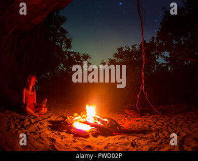 Silhouette d'girl autour de feu de camp la nuit sur la rive du fleuve. Banque D'Images