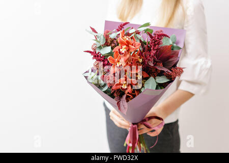 Bouquet de fleurs d'orchidées et de fleurs différentes. Jeune fille tenant une avec différents arrangements de fleurs de couleurs. mur blanc. Banque D'Images