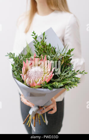 Bouquet luxuriant de King Protea, eucalyptus et d'autres verts. Jeune fille tenant une avec différents arrangements de fleurs de couleurs. mur blanc. Banque D'Images