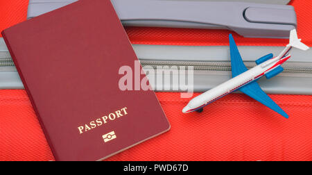 Le passeport et le petit avion sont laissés sur la valise de voyage rouge. Banque D'Images