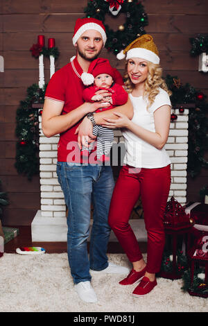 Heureux assis près de la famille élégante cheminée avec petit-fils et mignon chien et souriant. Les parents et l'enfant dans la famille Santa regardez, chien à tête rouge. Fe Banque D'Images