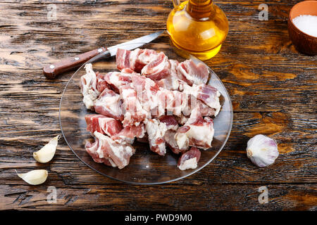 Couper la viande de porc cru réside dans une assiette sur une table en bois. à côté de l'épices et d'huile d'olive Banque D'Images