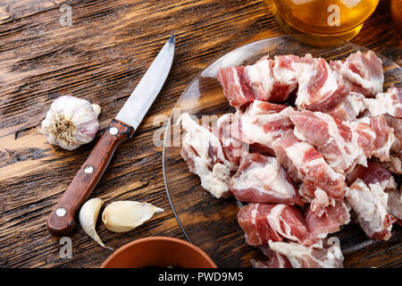 Couper la viande de porc cru réside dans une assiette sur une table en bois. à côté de l'épices et d'huile d'olive Banque D'Images