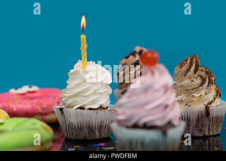 Studio close-up of delicious cupcakes et donuts avec un anniversaire candle burning contre fond bleu pour copy space Banque D'Images