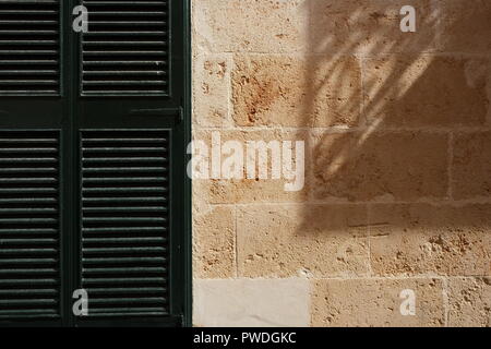 Volet en bois et une forte ombre jetée sur mur de pierre Ciutadella Menorca Espagne Banque D'Images