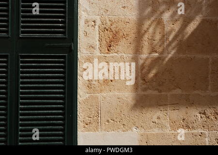 Volet en bois et une forte ombre jetée sur mur de pierre Ciutadella Menorca Espagne Banque D'Images