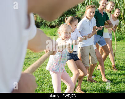 Smiling kids avec les mères et les pères jouer remorqueur de la guerre durant les jeux en plein air aux beaux jours Banque D'Images