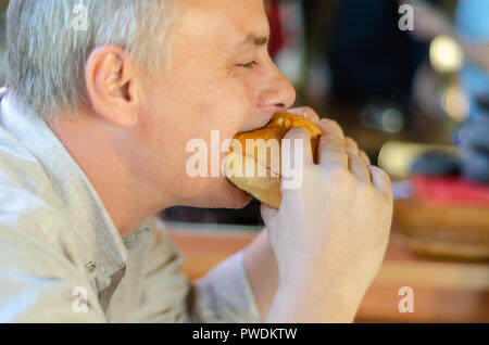 L'homme avec plaisir bites un appétissant burger dans un steak house restaurant. Banque D'Images