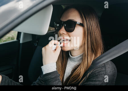 Cute young girl peintures pilote lèvres à l'intérieur de la voiture. Banque D'Images