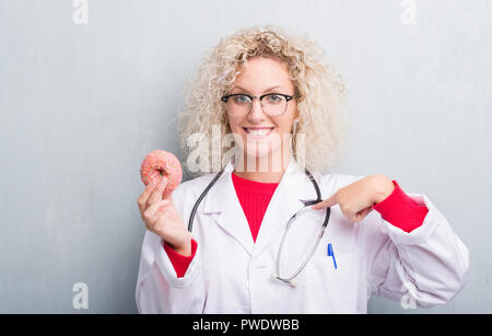 Jeune blonde dietist médecin femme de plus grunge grey wall eating avec surprise face à face à lui-même Banque D'Images