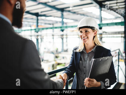 Un portrait d'une femme et homme méconnaissable ingénieur dans une usine, se serrer la main. Banque D'Images