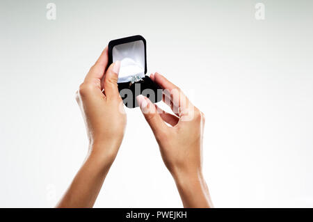 Modèle féminin les mains avec une bague de fiançailles en or blanc platine avec un diamant taille émeraude et Baguettes dans une boîte de bijoux Banque D'Images