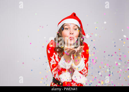 Maison de vacances de Noël, et les gens concept - belle et jeune femme en costume père noël sur fond blanc souffle sur confetti Banque D'Images