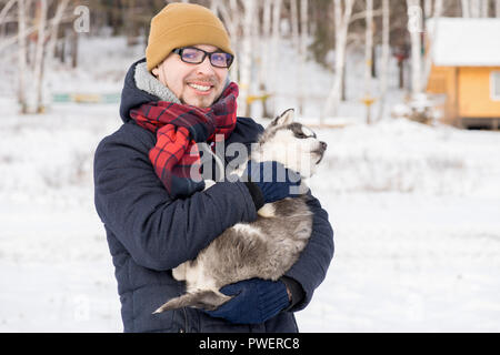 Taille portrait de jeune homme moderne smiling at camera tout en maintenant le chiot Husky mignon à l'extérieur en hiver, copy space Banque D'Images