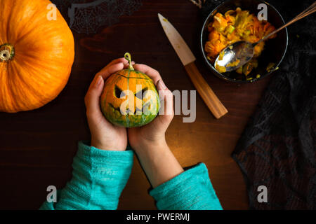 Photo de mains tenant jack-o-lanterne citrouille de assis à table en bois Banque D'Images