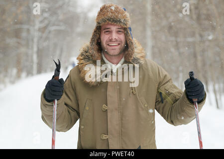 Waist up portrait of happy young man smiling at camera tout en appréciant le ski en forêt d'hiver enneigé Banque D'Images