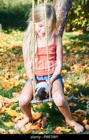 Cute child girl sitting on swing dans le jardin et jouer avec cochon d'animal de compagnie Banque D'Images