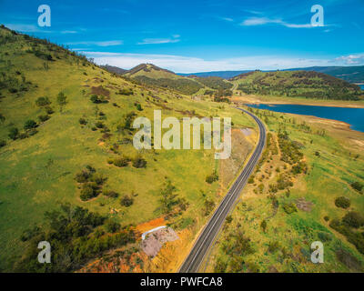 Chemin rural en passant par les collines verdoyantes et le lac pittoresque paysage - antenne Banque D'Images