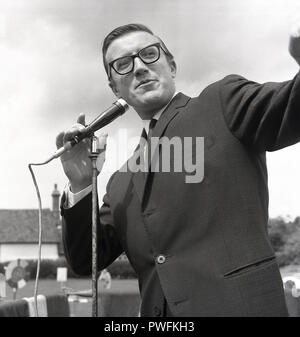 1967, l'artiste anglais, danseur, chanteur, musicien, présentateur de télévision et de charité, Roy Castle sur le micro à une fête du village, Buckinghamshire, Angleterre, Royaume-Uni. Un trompettiste de jazz accompli, Roy Castle était un acteur et interprète extrêmement versatile et parmi ses nombreux crédits a été son rôle dans la présentation de la longue et populaire de la télévision pour enfants, la série 'Record Breakers'. Banque D'Images