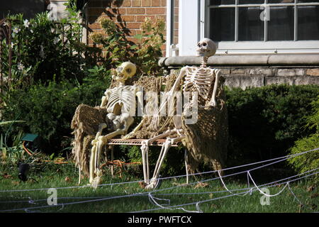 Un couple de squelettes assis sur un banc comme décorations halloween affiché sur la pelouse comme une célébration d'une maison de vacances d'automne. Banque D'Images