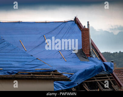La bâche de protection sur le toit s'agite à la tempête avec pluie. La toile couvre le toit de la vieille maison à la reconstruction. Banque D'Images
