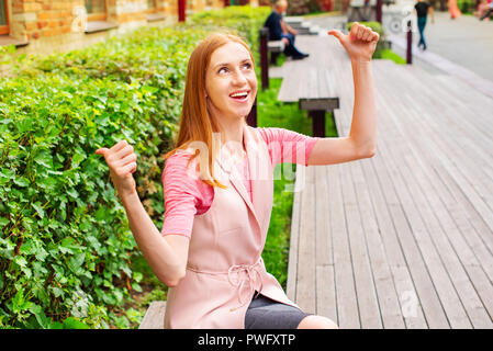 Belle jeune fille assise sur un banc en bois à l'air libre se réjouit. Journée ensoleillée buissons verts vie focus sélectif copy space Banque D'Images