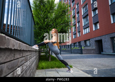 Jeune femme gymnaste avec un slim figure dans les vêtements de sport faisant s'étendant sur une rue de ville sur une chaude journée d'été. S'étendant à l'air libre Banque D'Images