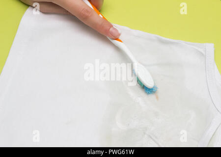 Fille nettoie la tache sur la chemise de l'enfant avec un pinceau à l'aide d'un détachant, close-up, de l'eau de javel Banque D'Images