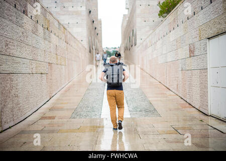 Homme marchant avec sac à dos avec trépied entre les bâtiments élevés en temps de pluie Banque D'Images